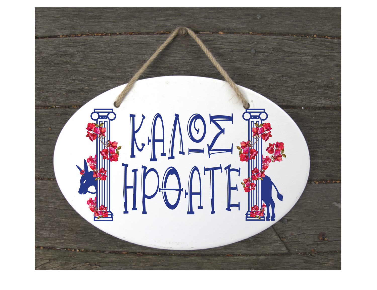 A decorative ceramic plaque with a white background, featuring blue Greek text and red floral designs, hanging by a wooden wall.