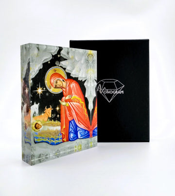 An icon depicting the Nativity of Christ, with intricate detailing and a 3D effect, placed next to its black cover with the Monogram Atelier logo.