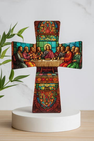 Decorative cross with stained glass design of the last supper on a white pedestal against a light background