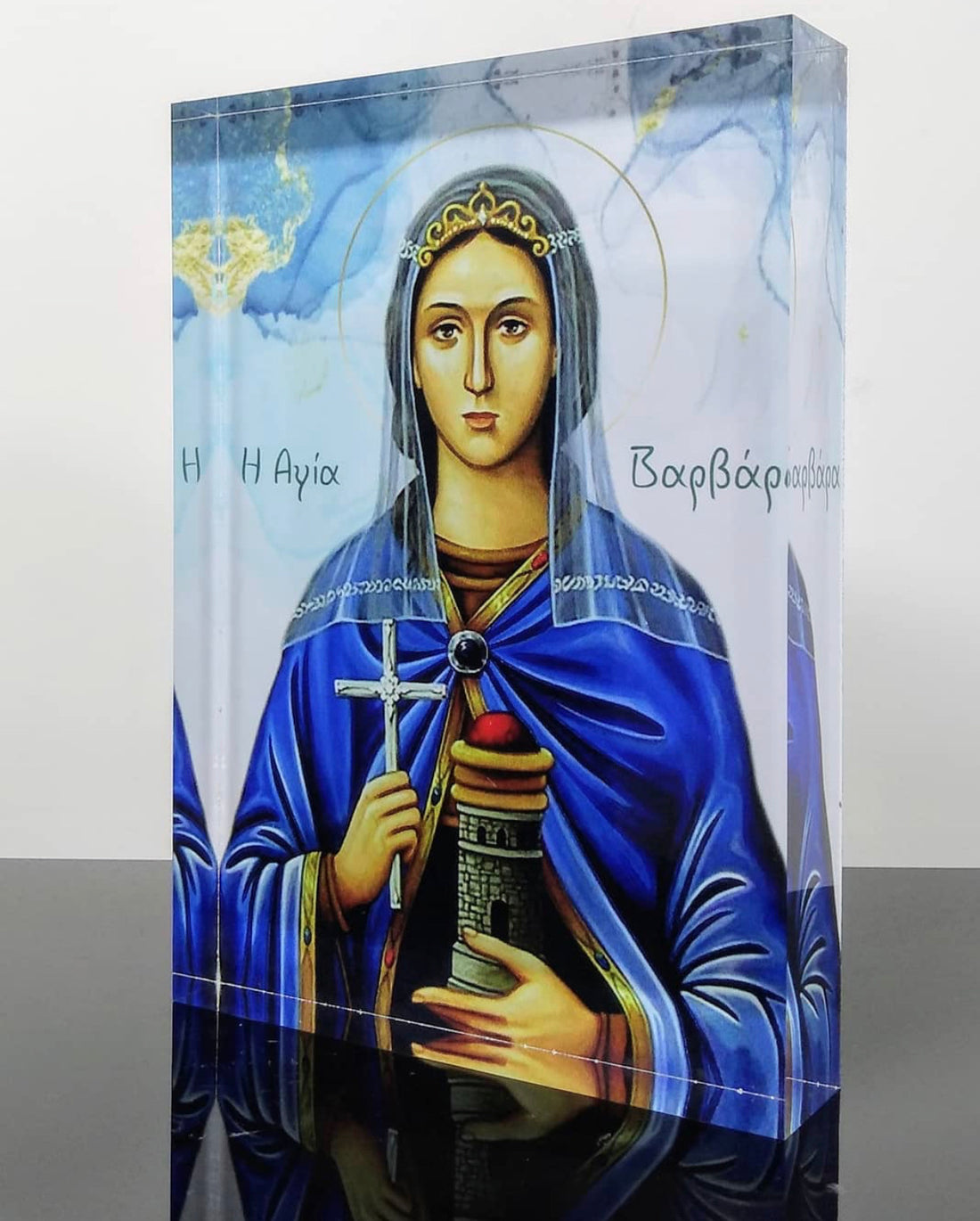 A handcrafted icon of Saint Barbara, featuring a female figure in blue robes with a halo, holding a cross, designed with a 3D effect on plexiglass.