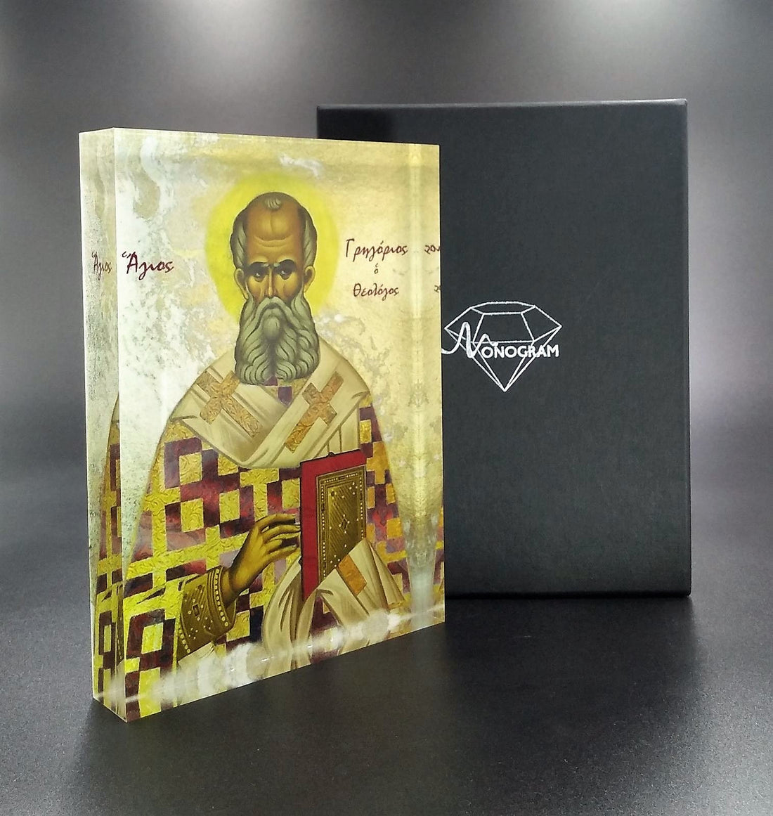 An icon of Saint Gregory the Theologian, featuring a man with a beard and mustache, wearing a white and gold robe, holding a book and a cross, with a 3D effect.