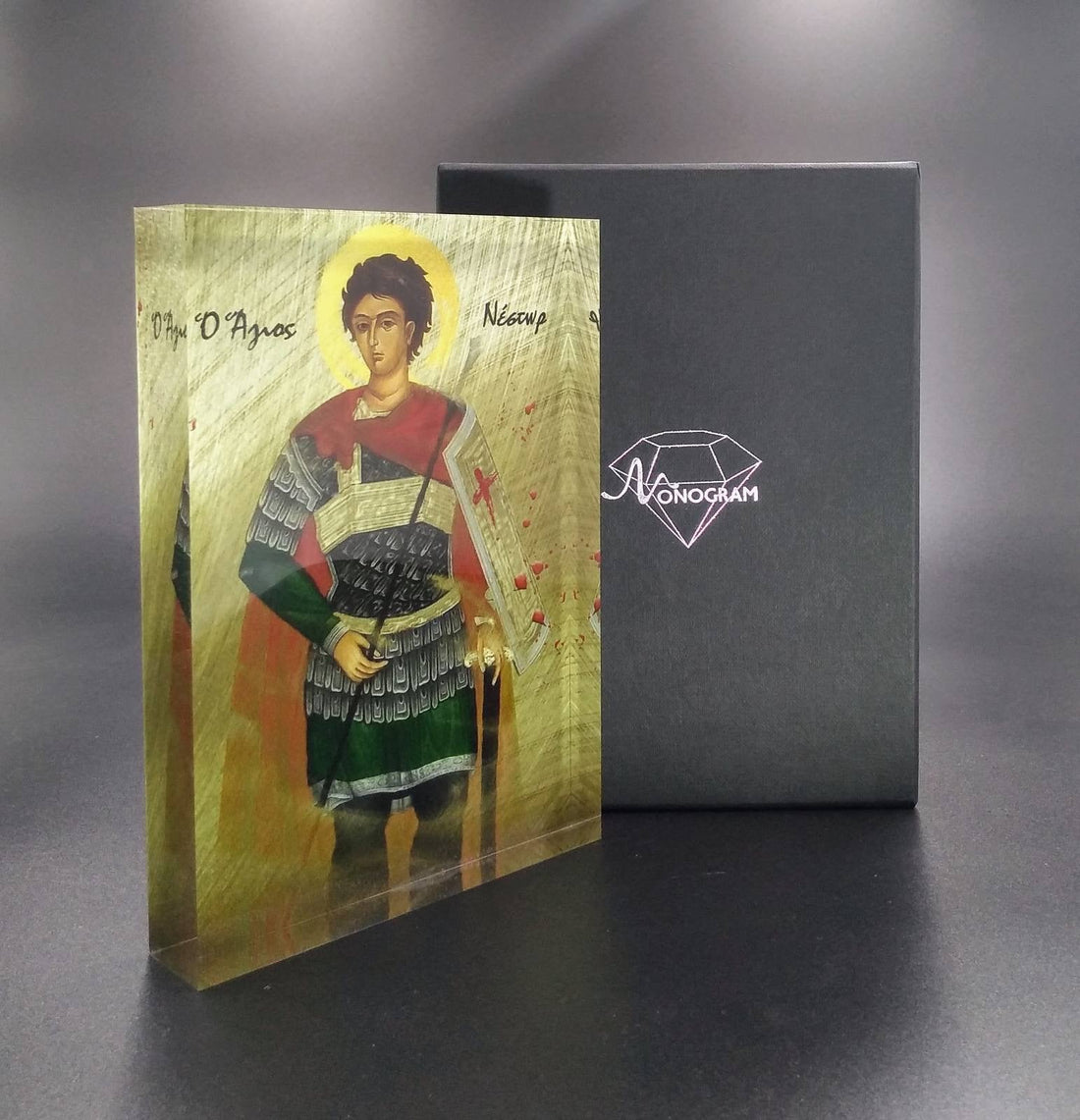A handcrafted icon of Saint Nestor, featuring a figure with a halo, dressed in traditional attire, holding a book, and standing against a golden background.