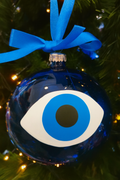 Decorative ornament with an eye design on a blue background, hanging on a Christmas tree.