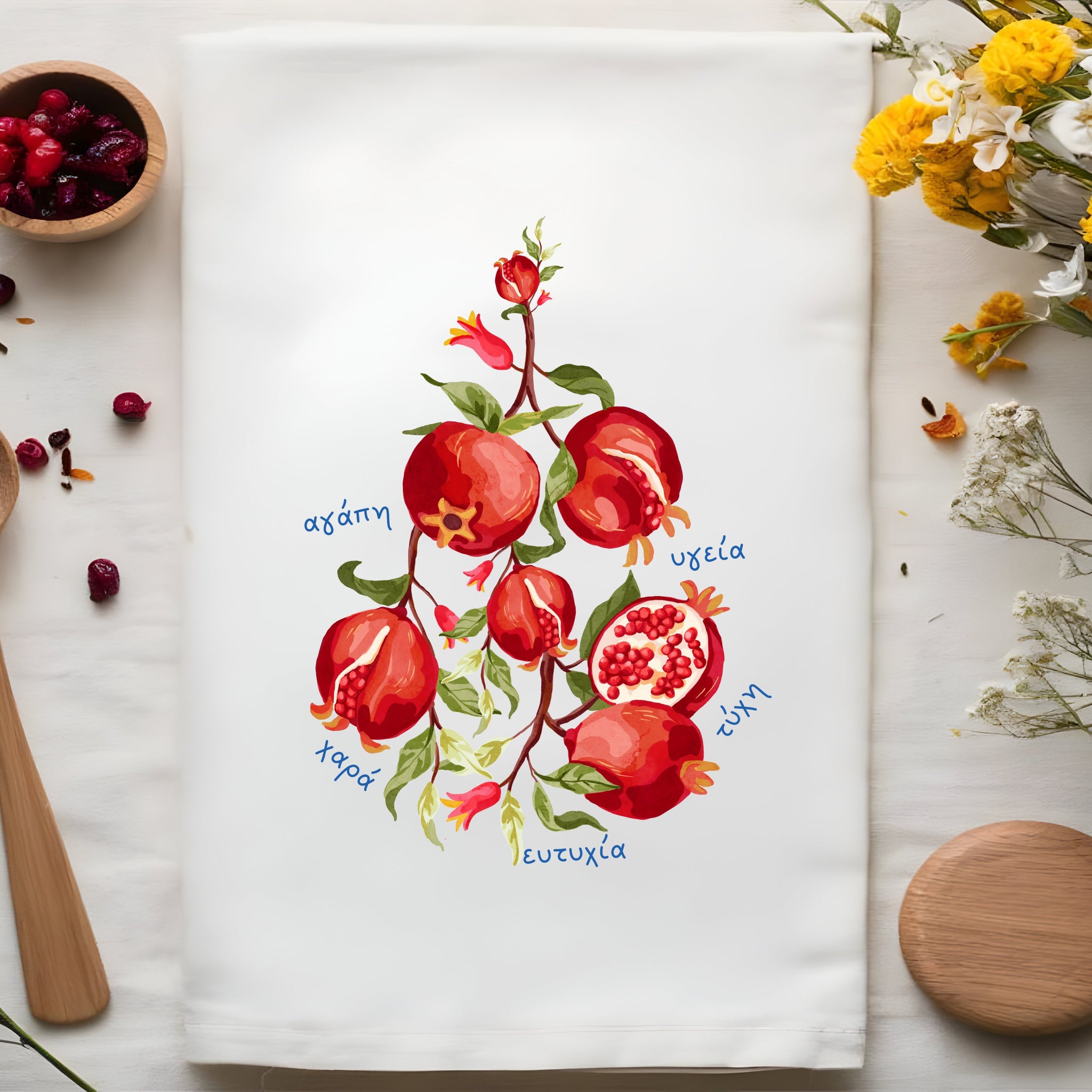 GreeknTea towel with pomegranate design, wooden spoon, and flowers on a white surface