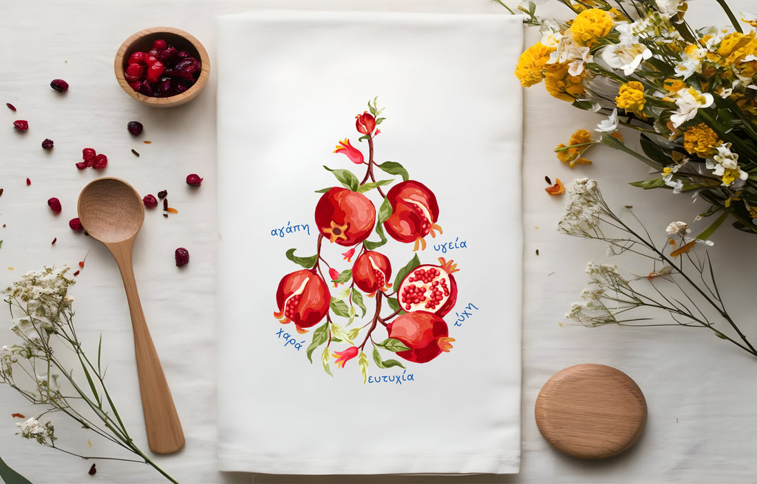 GreeknTea towel with pomegranate design, wooden spoon, and flowers on a white surface