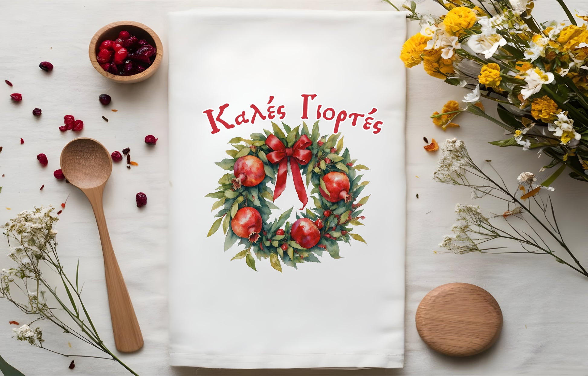 Decorative towel with wreath design and 'Kales Giortes' text, surroundeed by pomegranates
