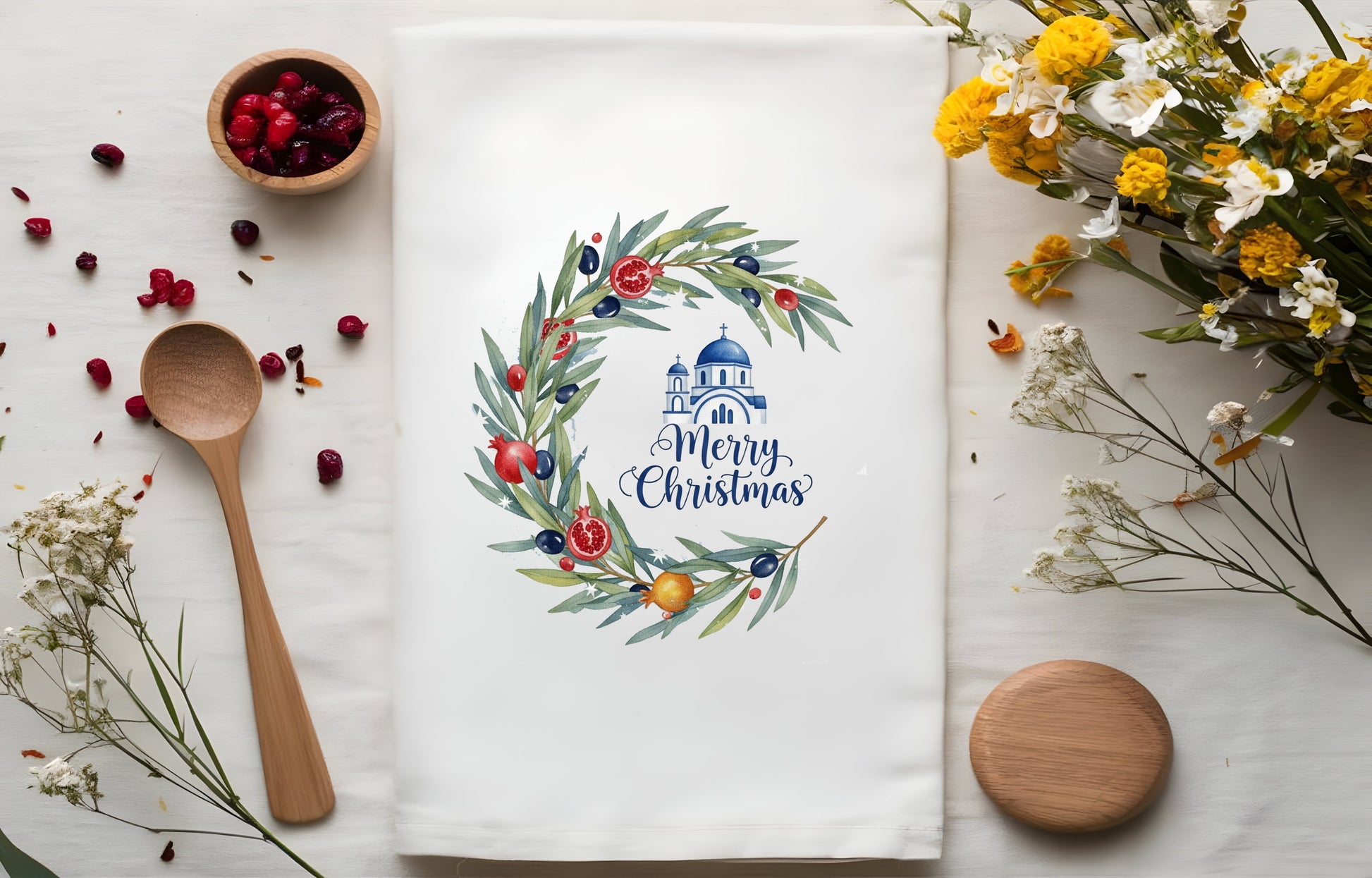 Christmas-themed towel with wreath and Santa Claus design, surrounded by wooden spoon, berries, and pomegrantes on a white background.