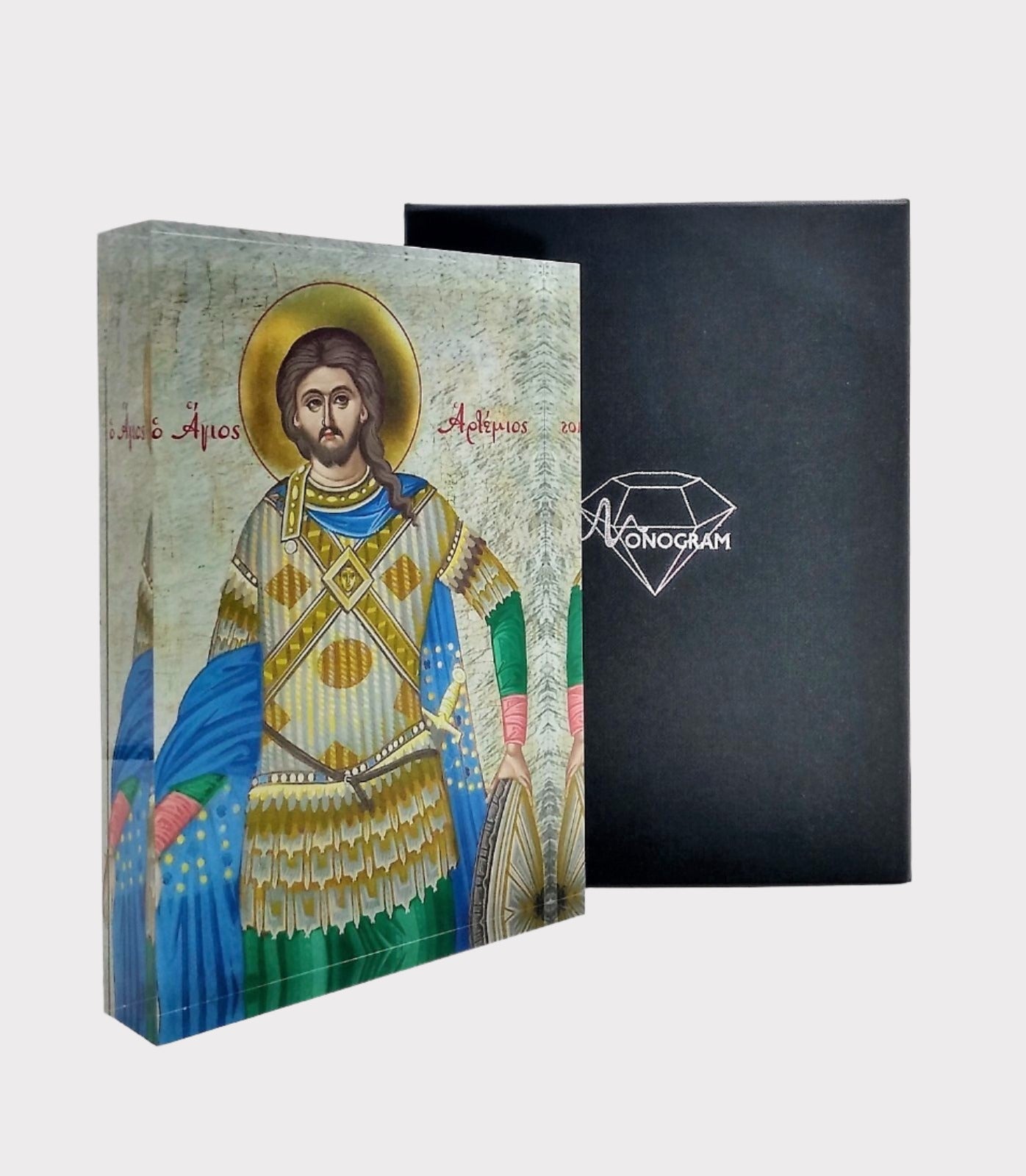 A hand-painted icon of Saint Artemios, depicted in a vibrant blue and gold robe, mounted on a black plexiglass cover with a decorative diamond-shaped logo on the front.