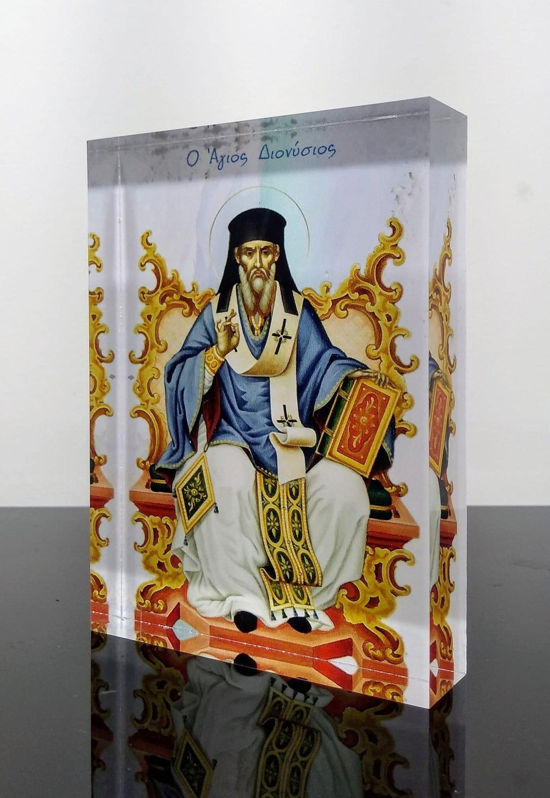 A colorful icon of Saint Dionysios, featuring the figure in a detailed robes seated on a golden throne, set within a plexiglass frame.