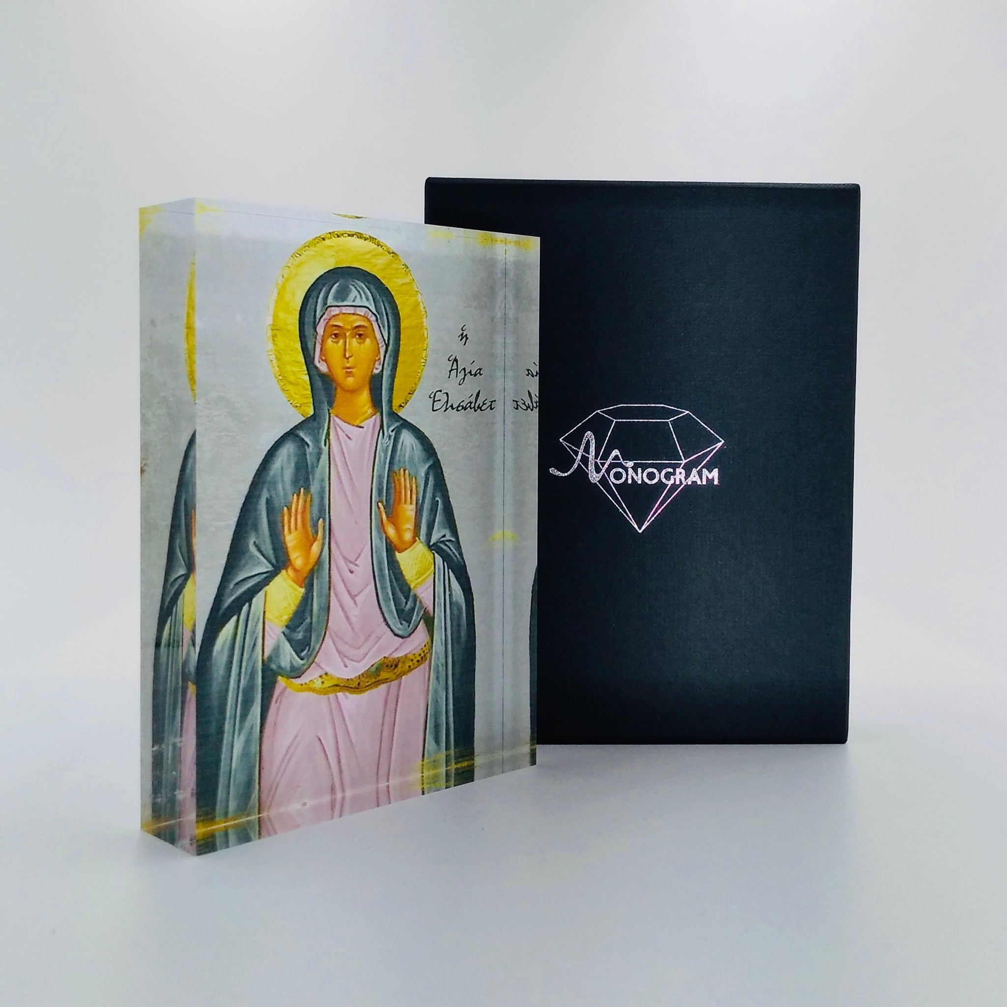 An icon of Saint Elizabeth, also known as the Blessed Virgin Mary, with a 3D effect, placed next to its black cover with the Monogram Atelier logo in pink.