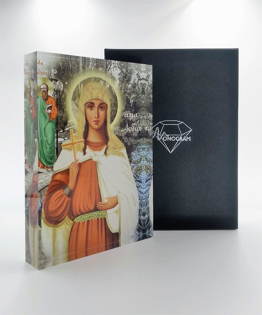 A handcrafted icon of Saint Lydia, with a 3D effect, made of plexiglass, placed next to its black packaging with the brand name 'Monogram Atelier' visible.