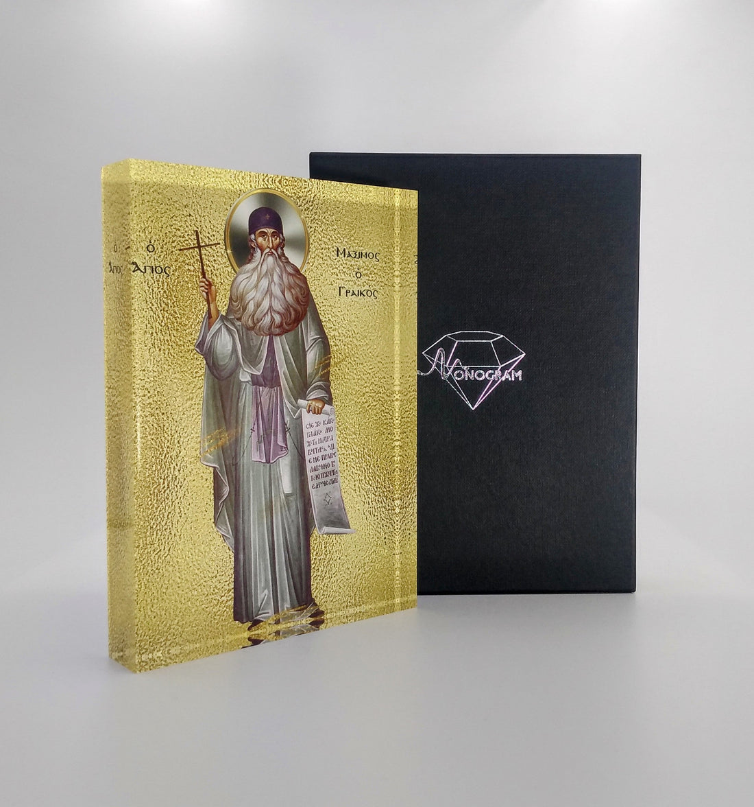 An icon of Saint Maximus the Confessor, depicted in a monastic robe holding a book, with a 3D effect on the cover, placed next to its black cover with a diamond-shaped logo.