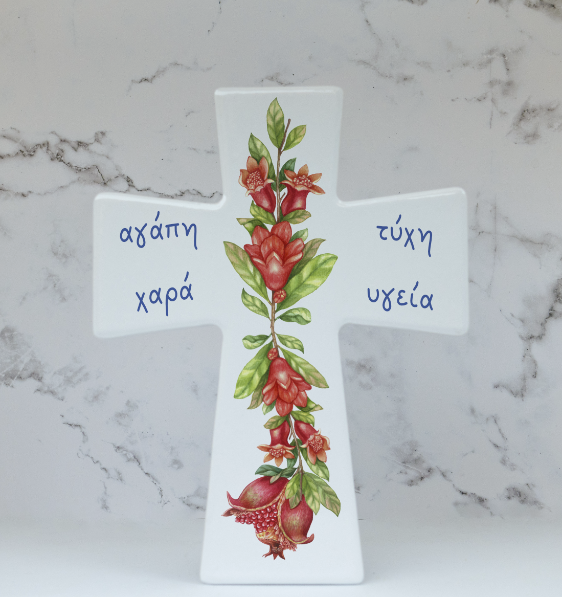 A ceramic cross with a floral design and Greek text, standing on a marble surface.