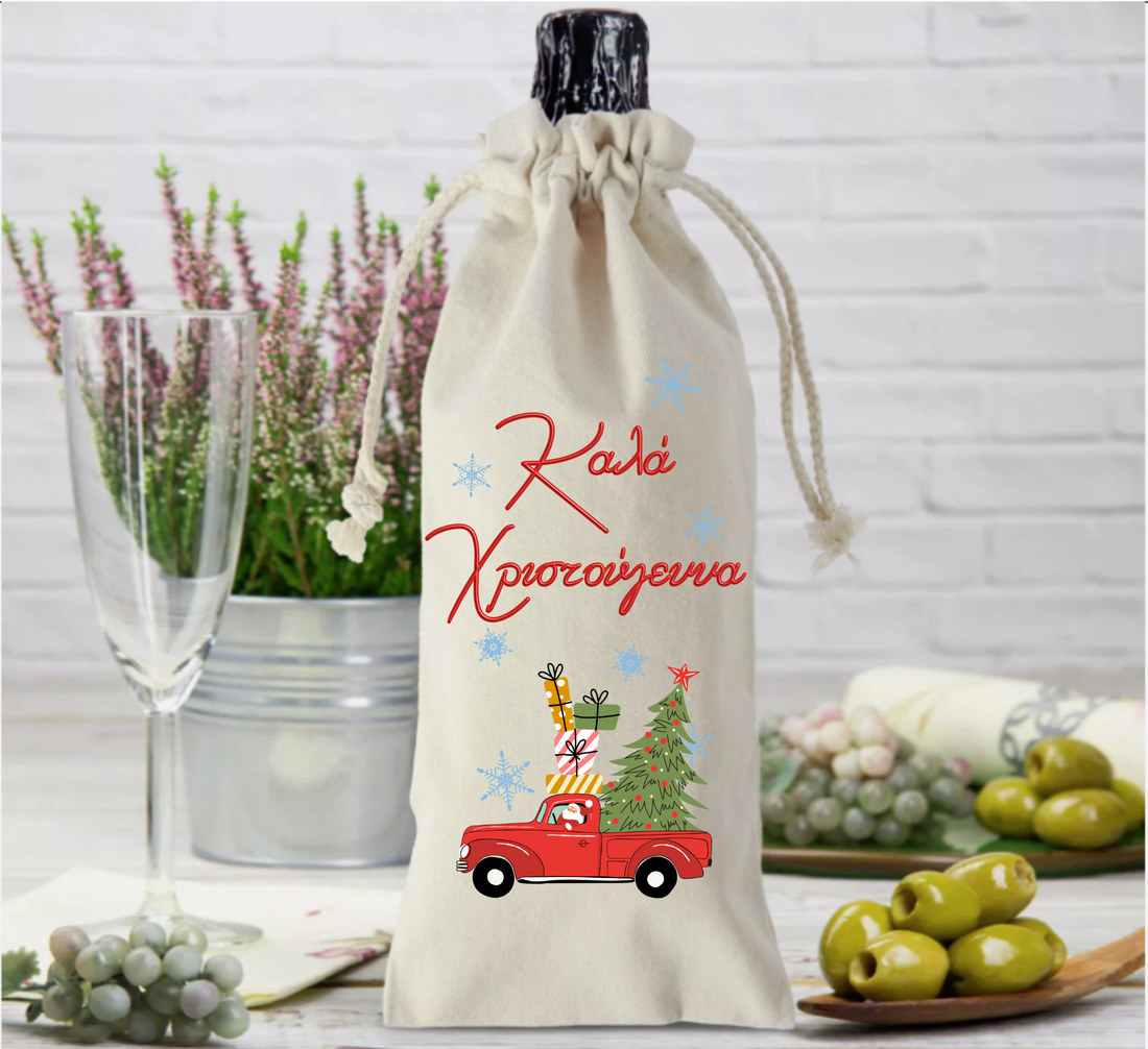 A beige fabric bottle bag with a Christmas themed graphic, including a red car, Christmas tree, and festive decorations, placed on a table with a glass of wine and some olives in the background.