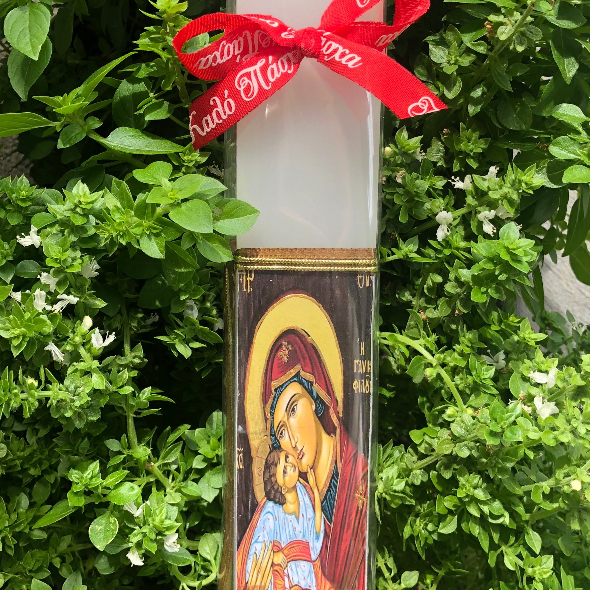 A decoupage Easter candle with a printed design featuring a religious icon, wrapped with a red ribbon.