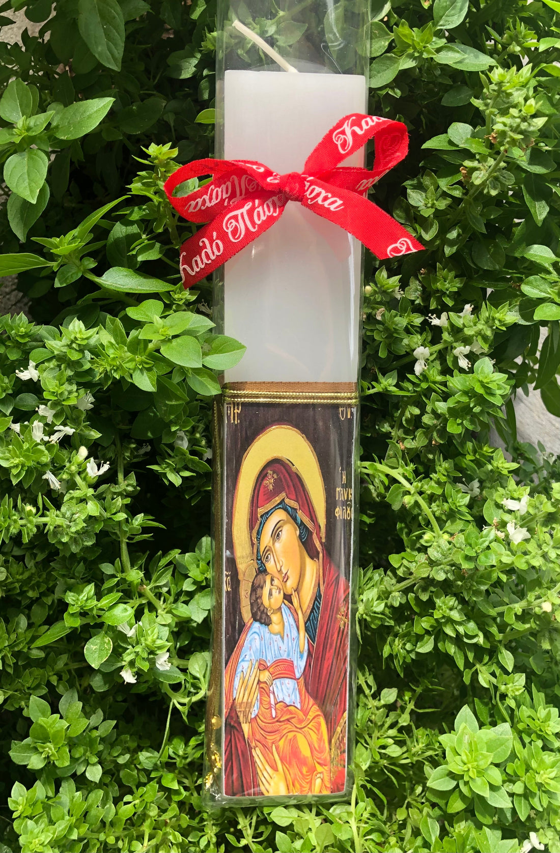 A decoupage Easter candle with a printed design featuring a religious icon, wrapped with a red ribbon.