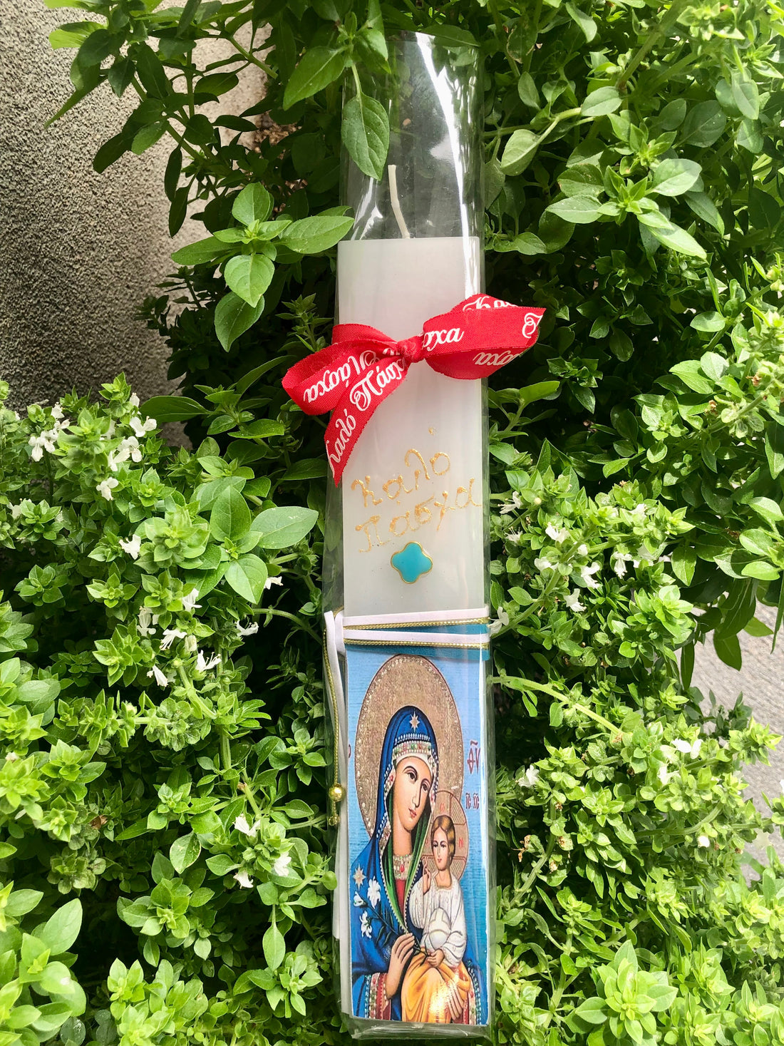 A decoupage Easter candle with a printed design featuring a religious icon, wrapped with a red ribbon.