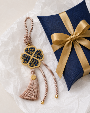 Four leaf clover lucky charm gouri with gold blue rhinestones, mocha cord, tassel, small 26 tag and gift box with gold ribbon.
