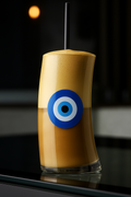 Glass of iced coffee or frappe with a blue evil eye mati on a dark background