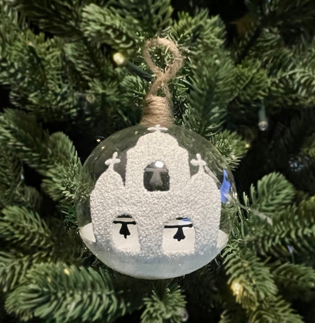 Hand-blown glass Christmas bauble with turquoise and white Greek churches hanging on green Christmas tree branches.