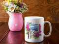 Greek ceramic mug with the word ‘Καλημέρα’ (Good Morning), featuring a painted Santorini village view framed by vibrant pink bougainvillea.