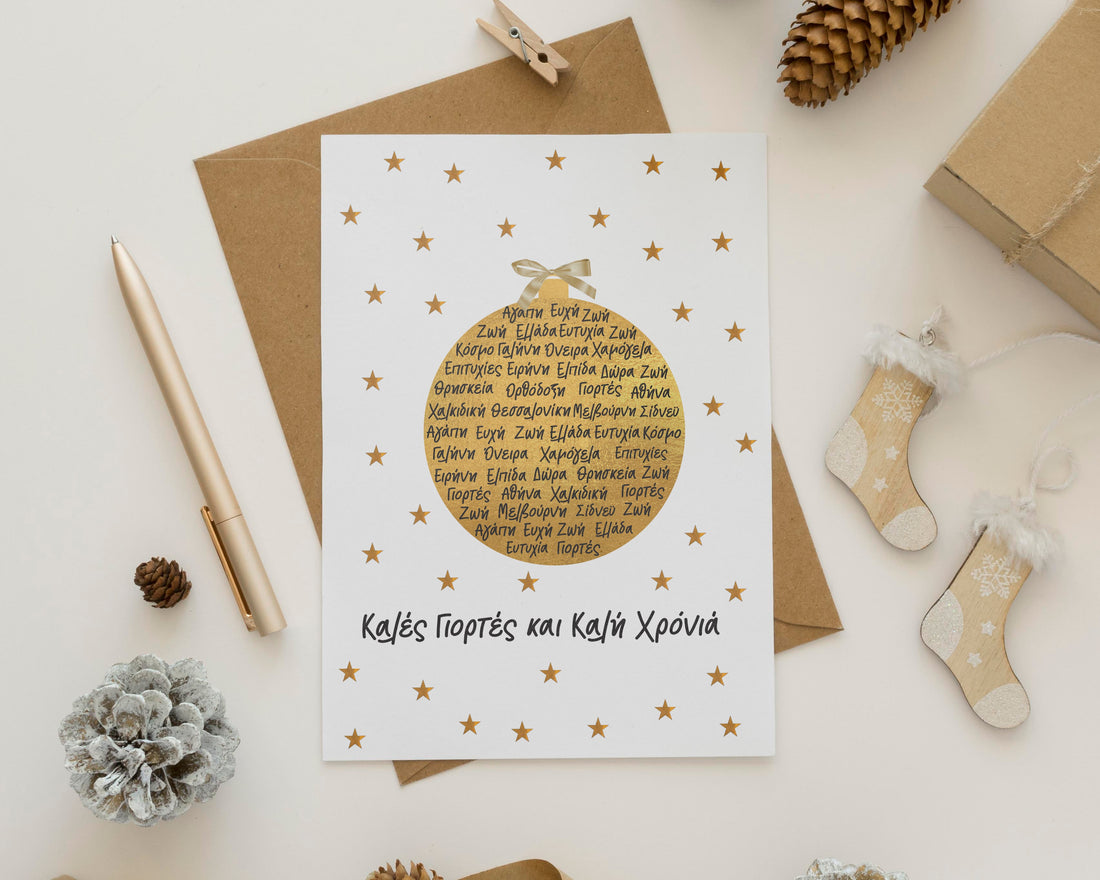 Gold foiled Christmas card with a message in Greek, accompanied by an envelope and decorative elements like pine branches and presents in the background.
