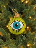 Lime green hand-blown glass evil eye Christmas bauble with painted turquoise eye, hanging on a festive Christmas tree.