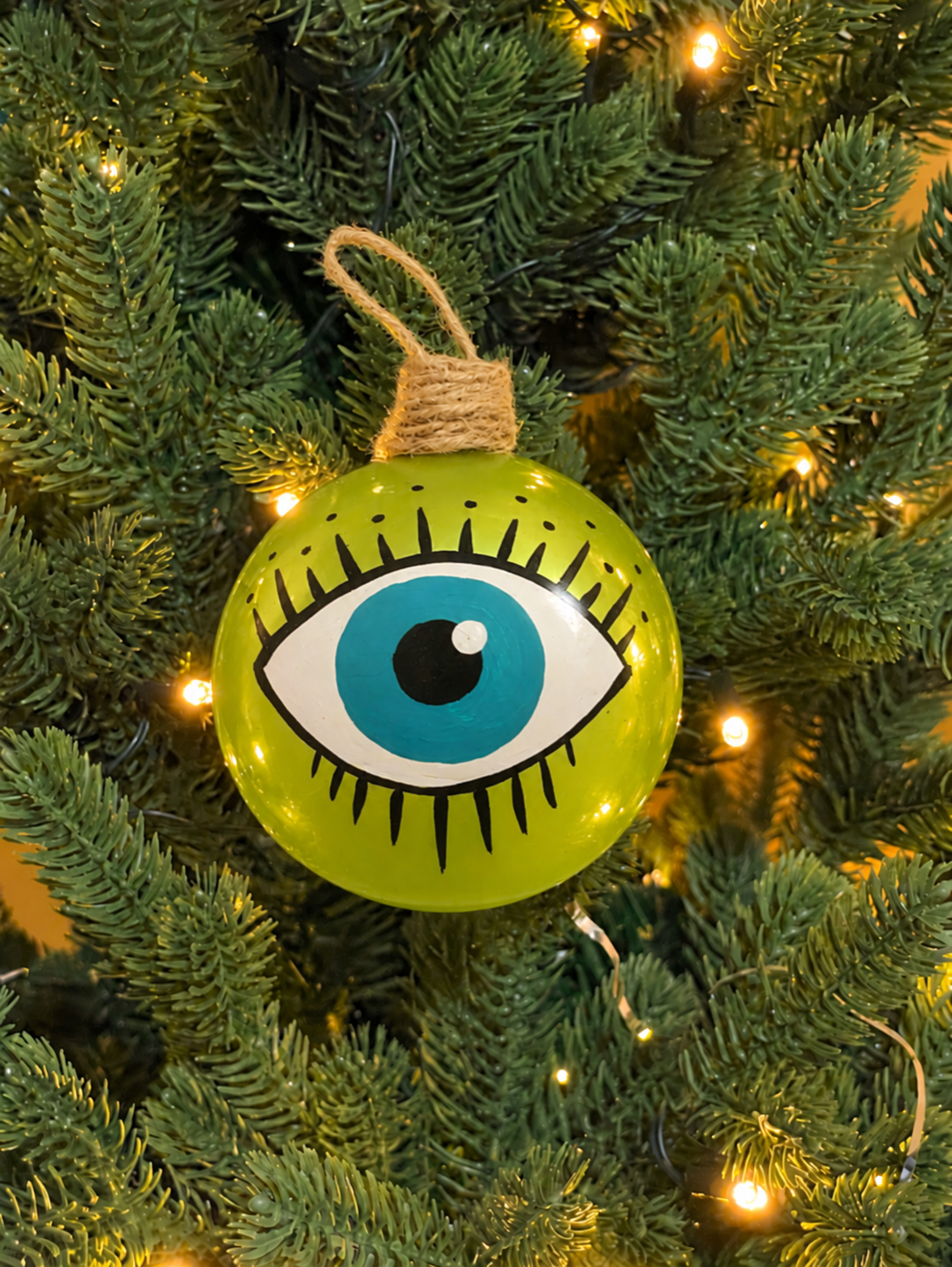 Lime green hand-blown glass evil eye Christmas bauble with painted turquoise eye, hanging on a festive Christmas tree.