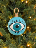 Sky blue Greek evil eye Christmas ornament with hand-painted eye and black eyelashes, displayed among Christmas tree lights.