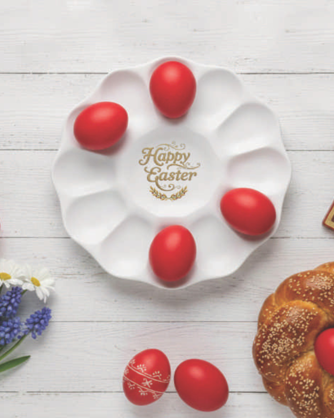 White 'Happy Easter' plate with red eggs on a wooden surface with flowers and bread.