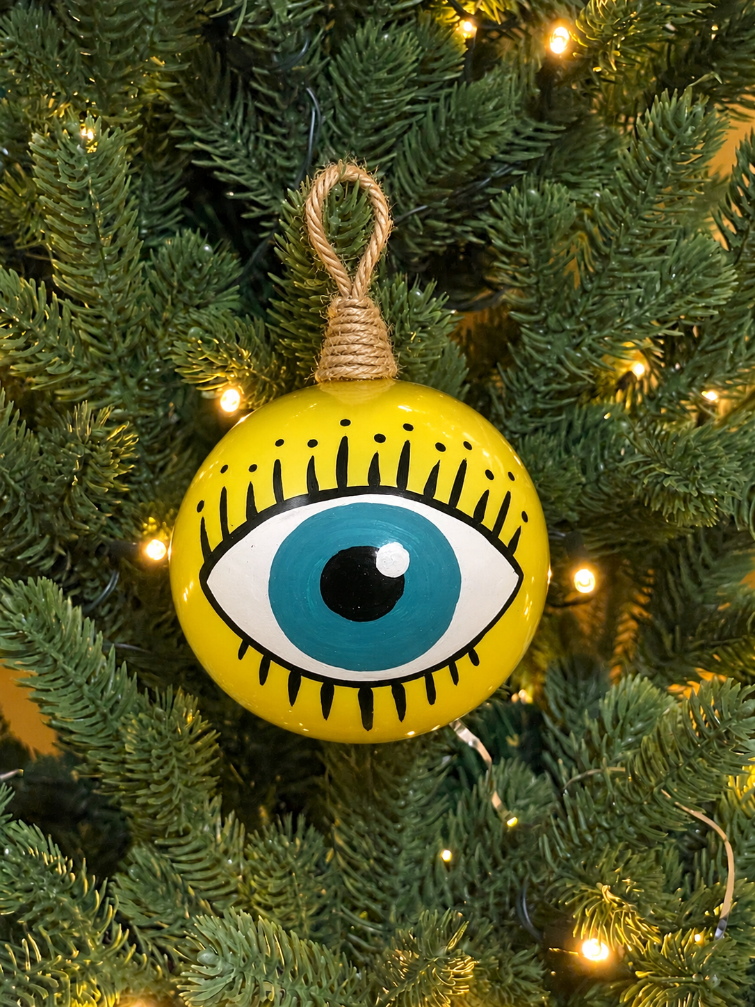 Sky blue Greek evil eye Christmas ornament with hand-painted eye and black eyelashes, displayed among Christmas tree lights.