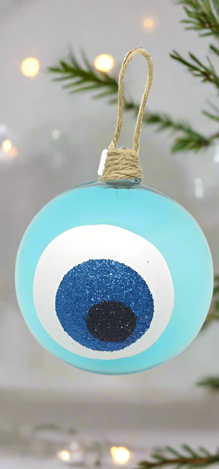 A turquoise round hand blown glass bauble with blue and white colors and a glittery finish, featuring an evil eye design, hanging from a twine.