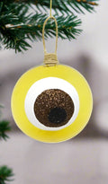 A yellow round hand blown glass bauble  hanging from a twine loop.