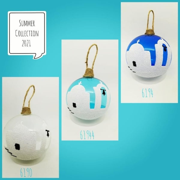 A hand blown glass bauble with a blue and white design, featuring a silhouette of a church, displayed against a green fern backdrop.