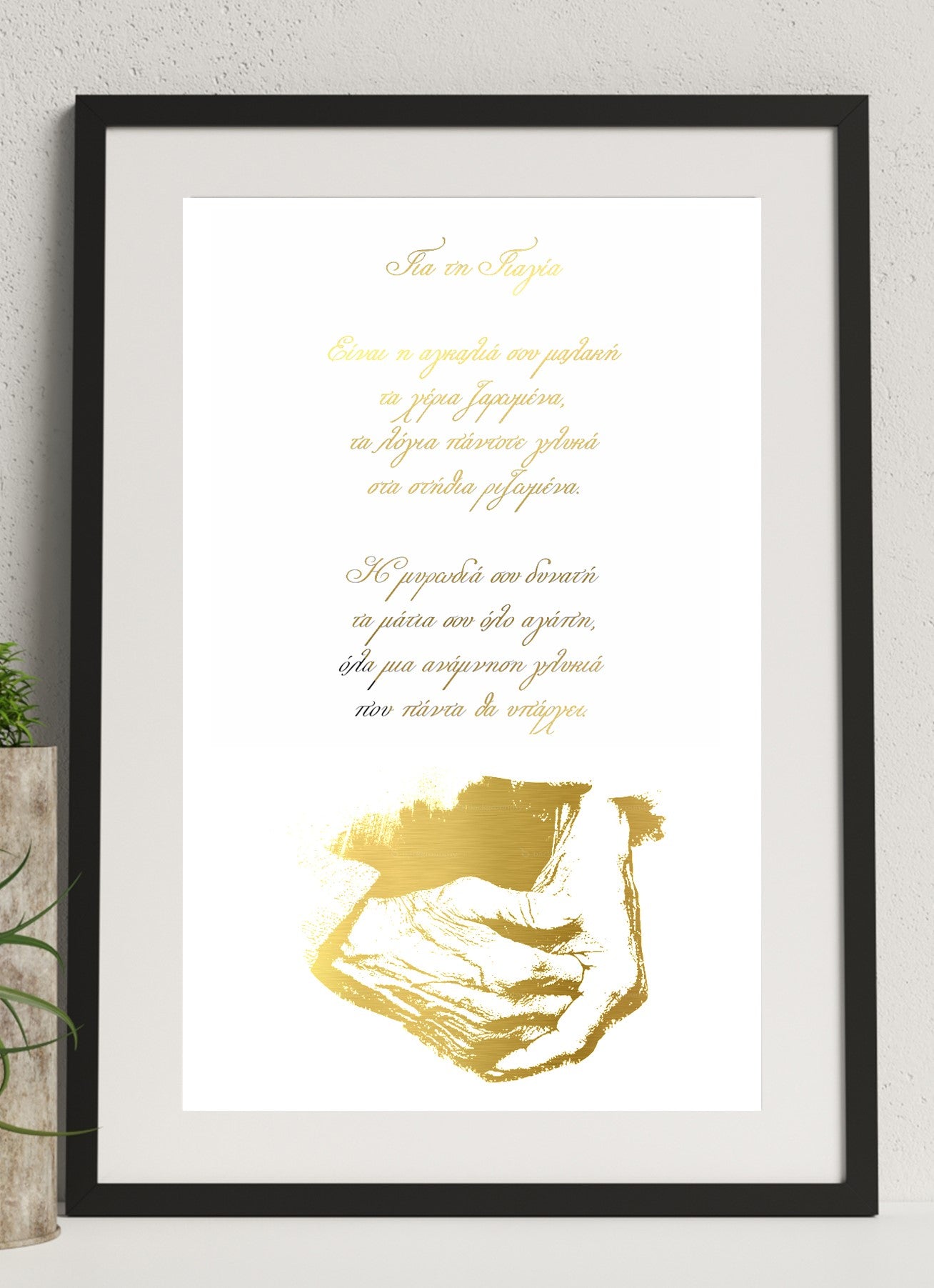 A framed print featuring a hand foiled design in gold for your grandmother in greek, displayed on a wall with a black frame and a small plant to the side.