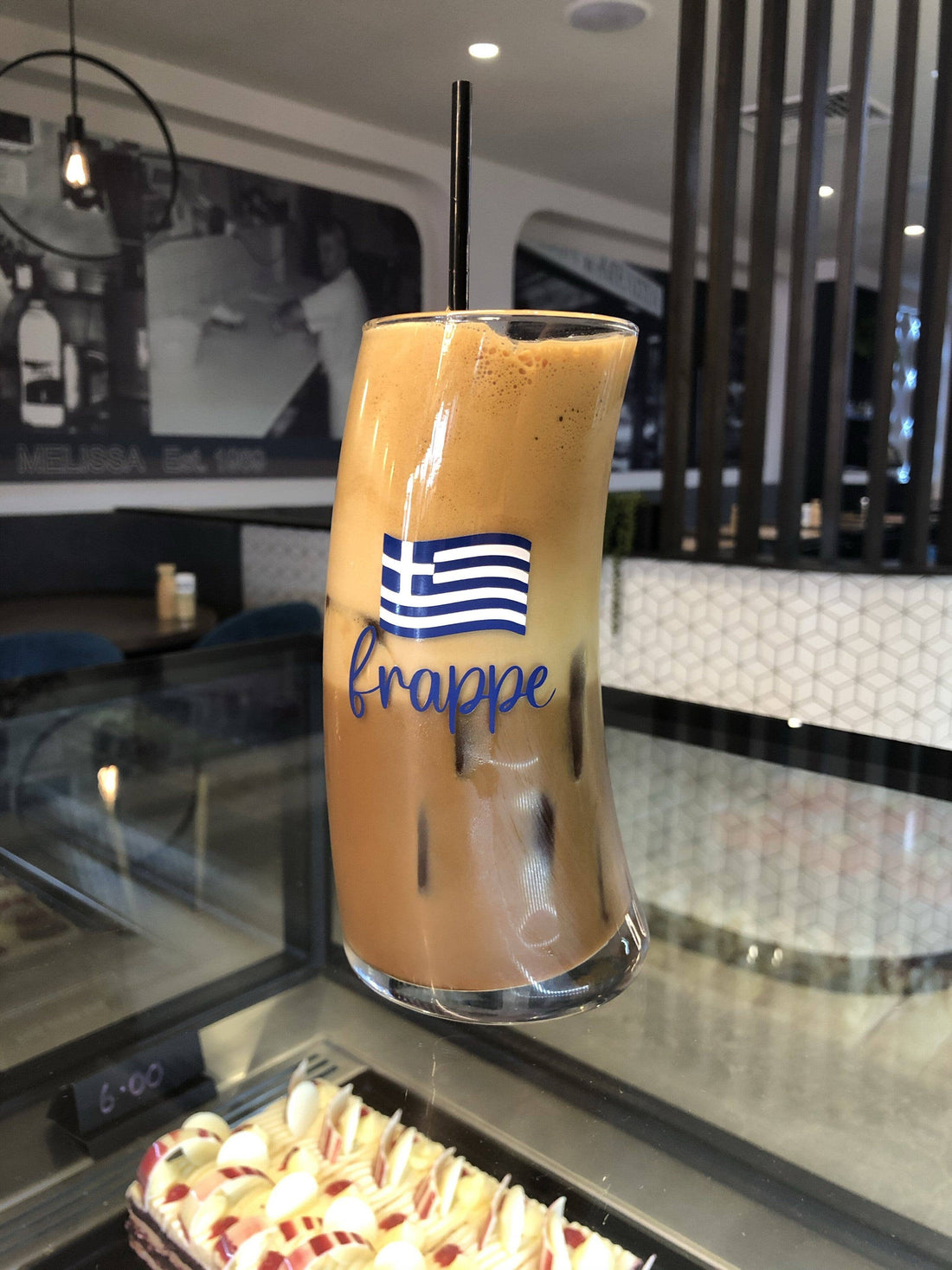 Original Wave Frappe Glass with Greek flag design, filled with iced Greek frappe at a café