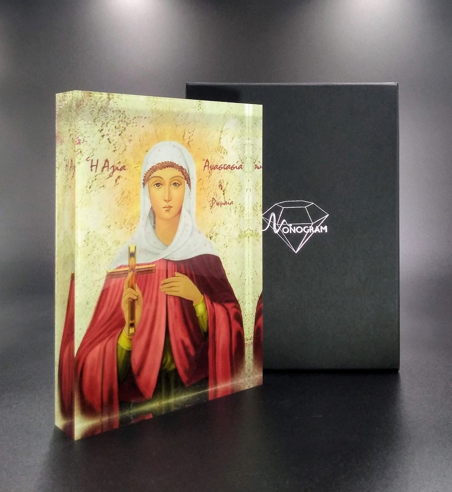 Orthodox plexiglass icon of Saint Anastasia Pharmakolytria displayed with branded Monogram Atelier gift box. Handmade Greek icon with healing cross and light textured backdrop.